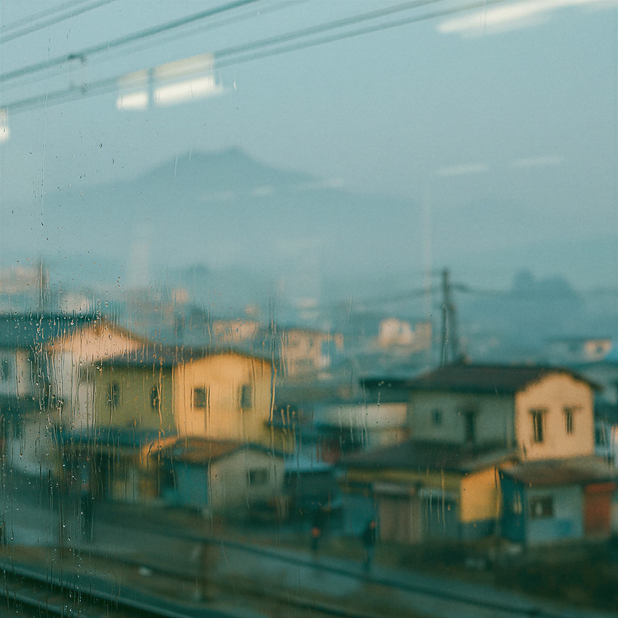 Rain-streaked train window looking out at a rural Japanese town at dawn, simulated photography created with Midjourney, stamped with VISID structured metadata